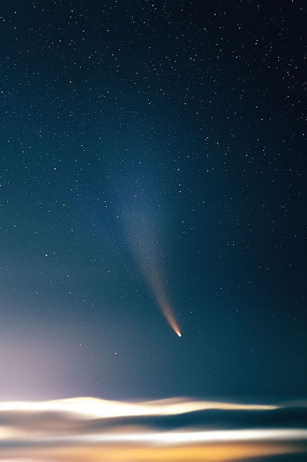 a comet floats in the night sky above a sea of clouds