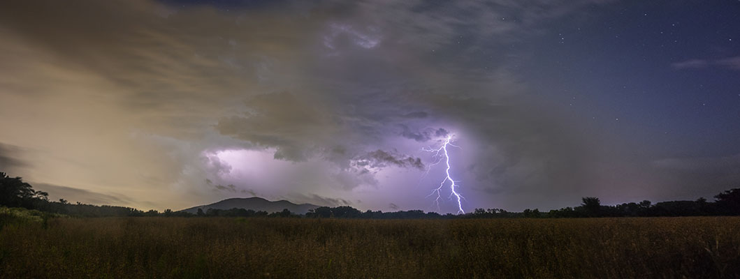 A panoramic shot with lightning on one end and stars on the other